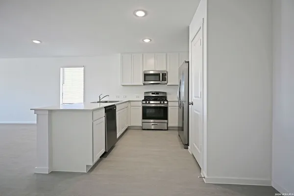 a living room with stainless steel appliances white cabinets and a refrigerator