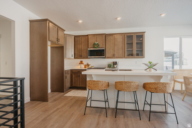 4595 North Fallow Way, Unit 511 Eagle Mountain, UT 84005 - Photo 15 of 32 Kitchen with a kitchen breakfast bar, wood finish cabinetry, glass insert cabinets, a kitchen island with sink, and light wood-style floors