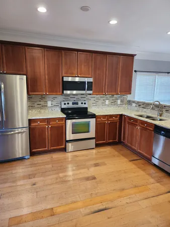 a kitchen with stainless steel appliances granite countertop a stove top oven a refrigerator and a sink with wooden cabinets