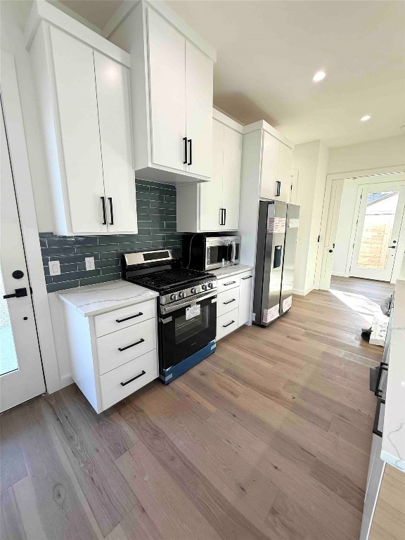 6809 Porter Street, Unit A Austin, TX 78741 - Photo 4 of 23 Kitchen with white cabinetry, stainless steel appliances, light wood finished floors, tasteful backsplash, and light stone countertops