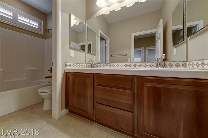 3144 Whitfeild Avenue Henderson, NV 89044 - Photo 29 of 55 Dual vanities with wood cabinetry and tile countertops complement this well-lit bathroom space.