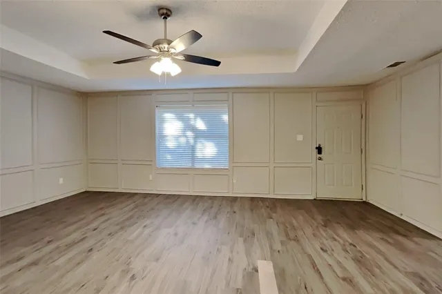 an empty room with wooden floor chandelier fan and windows