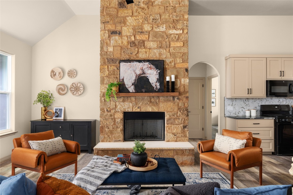Living room featuring wood finished floors, a stone fireplace, vaulted ceiling, and arched walkways