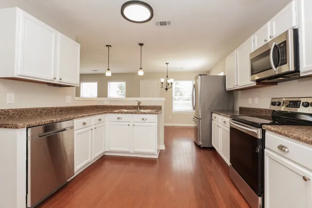 a kitchen with stainless steel appliances granite countertop a refrigerator a stove top oven a sink and dishwasher with wooden floor