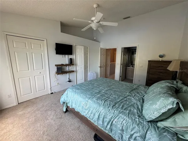 a spacious bedroom with a bed and a flat tv screen on the dresser
