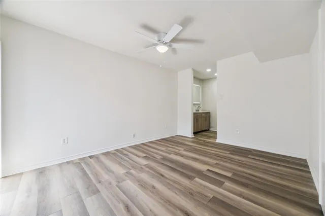 a view of an empty room with wooden floor and a ceiling fan