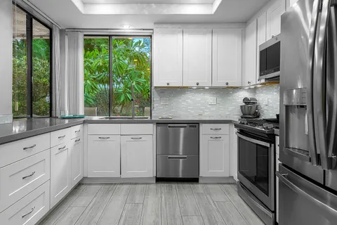 a kitchen with granite countertop white cabinets stainless steel appliances and a large window