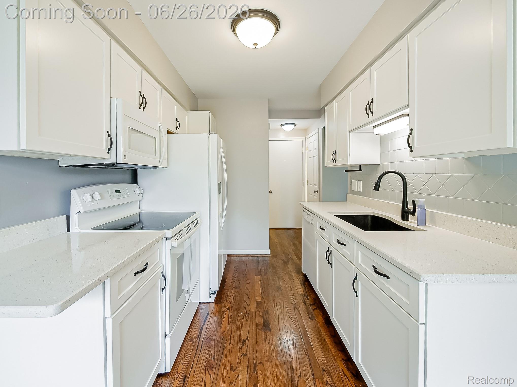 160 Pine Tree Ridge, Unit 3 Waterford, MI 48327 - Photo 5 of 26 Galley kitchen featuring white shaker cabinetry, light-toned countertops, hardwood-finish flooring, a black sink with a matte black faucet, and patterned tile backsplash