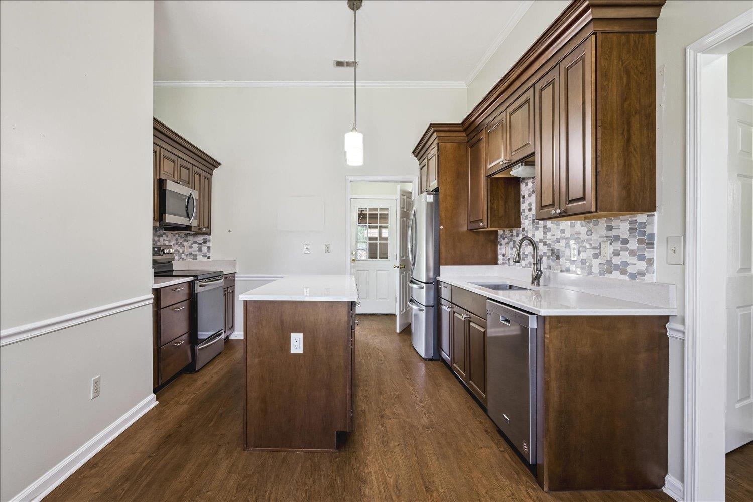 4654 Shadow Wick Lane Bartlett, TN 38002 - Photo 11 of 26 Kitchen featuring wood-finish flooring, white countertops, dark wood cabinetry with crown molding, stainless steel appliances, and a mosaic tile backsplash