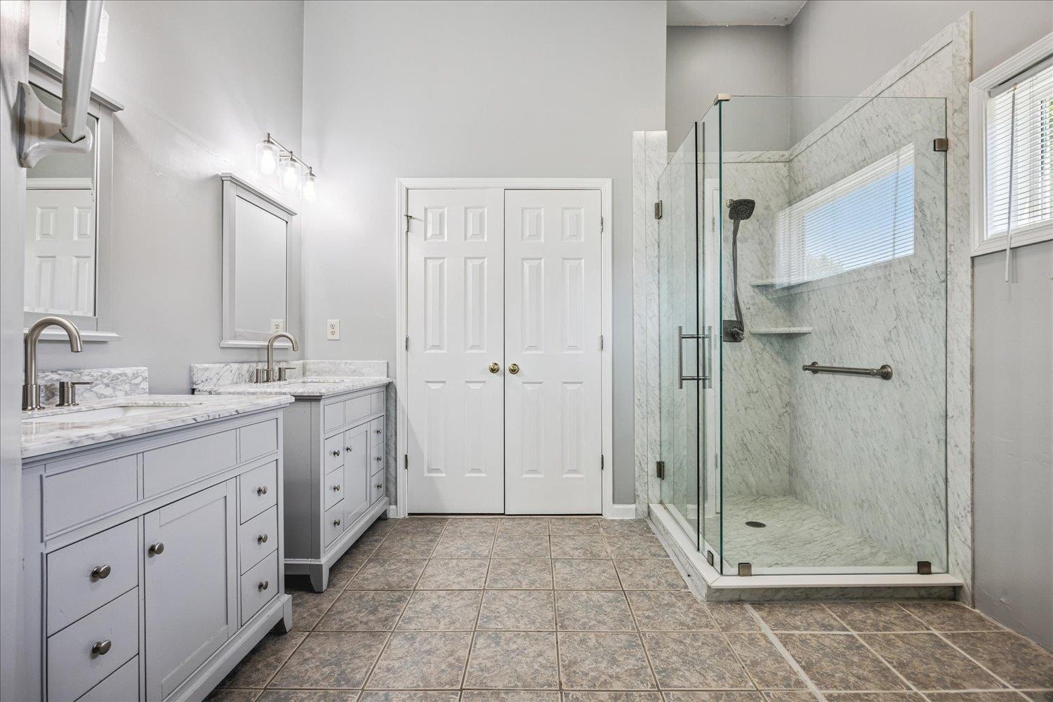 4654 Shadow Wick Lane Bartlett, TN 38002 - Photo 16 of 26 Modern bathroom featuring a spacious glass-enclosed shower with stone-finish walls, dual vanities with stone countertops, and tile flooring