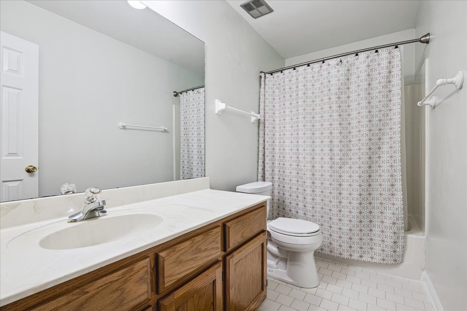 4654 Shadow Wick Lane Bartlett, TN 38002 - Photo 21 of 26 Bathroom featuring a single vanity with wood cabinetry and an integrated sink, a large wall-mounted mirror, a toilet, and a shower-over-tub combination with a shower curtain