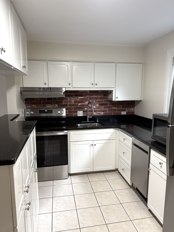 25 Lionel Avenue, Unit E Waltham, MA 02452 - Photo 5 of 13 a kitchen with granite countertop a stove a sink and a microwave