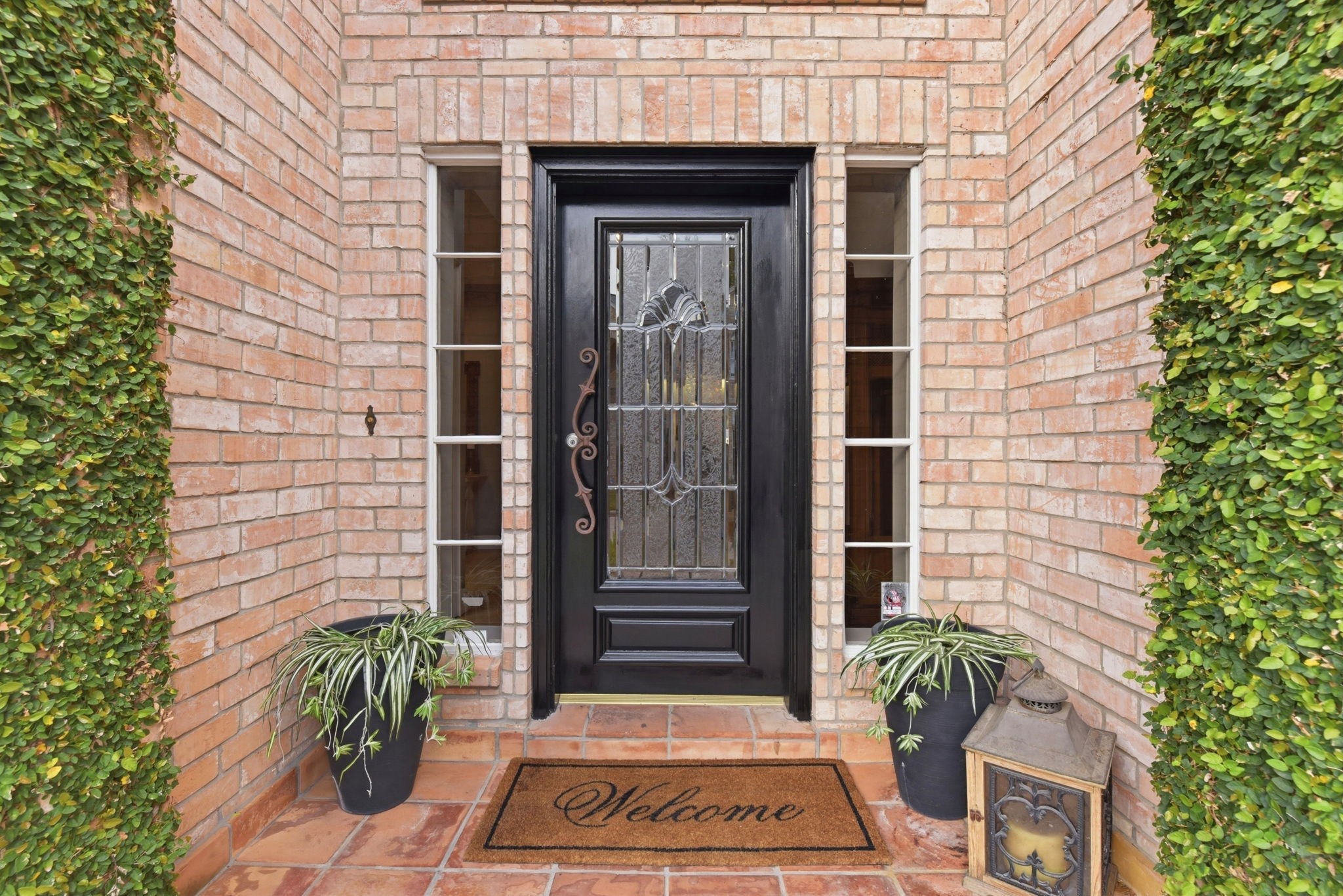 16322 Cranwood Drive Spring, TX 77379 - Photo 5 of 42 Welcome to your new home through a charming brick entryway, featuring a sophisticated black door framed by elegant side windows, lush greenery, and a warm welcome mat.