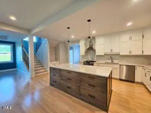 a kitchen with stainless steel appliances granite countertop a stove a sink and white cabinets with wooden floors