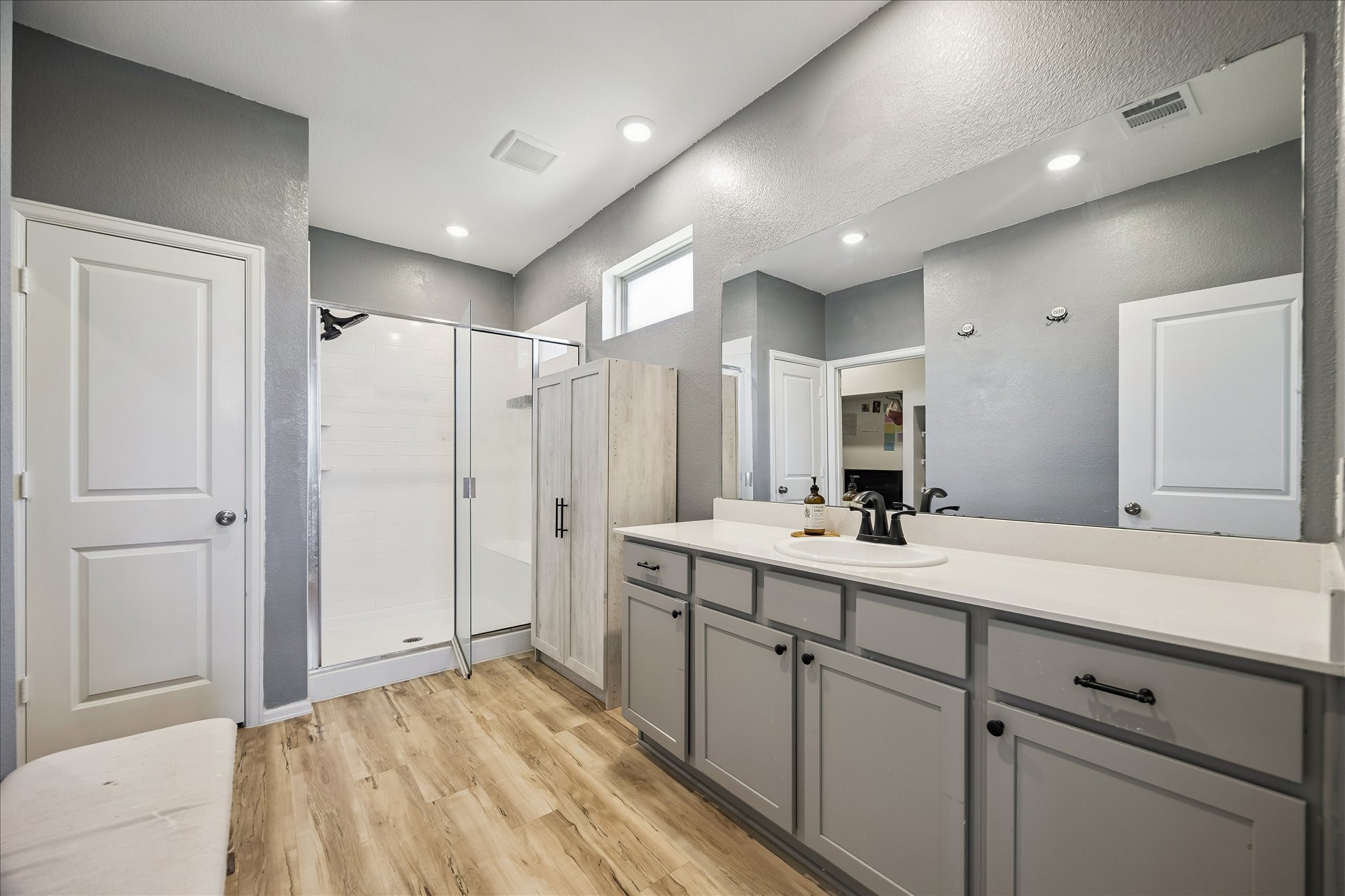3812 Moss Hl Road Rosenberg, TX 77469 - Photo 13 of 20 This bathroom features a modern design with sleek gray walls, a large mirror, and ample lighting. It includes a spacious walk-in shower, stylish cabinetry, and wood-style flooring, creating a refreshing and contemporary atmosphere.