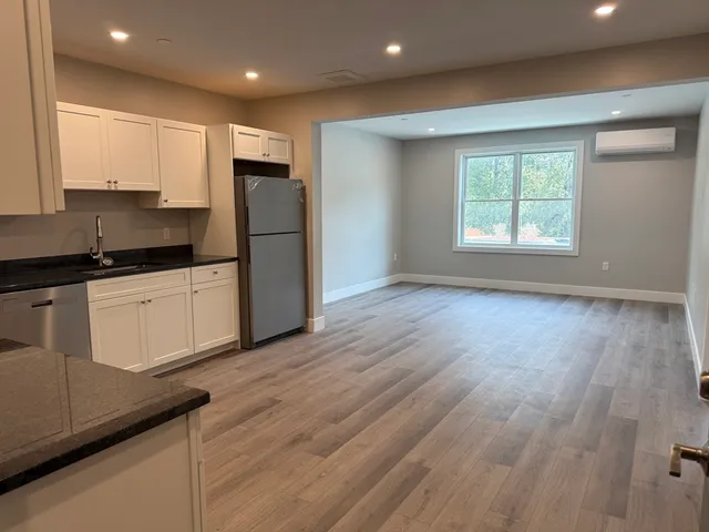 a kitchen with granite countertop a refrigerator a sink and white cabinets