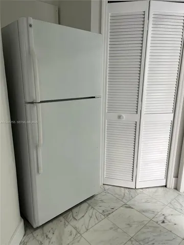 a view of a refrigerator in kitchen and an empty room