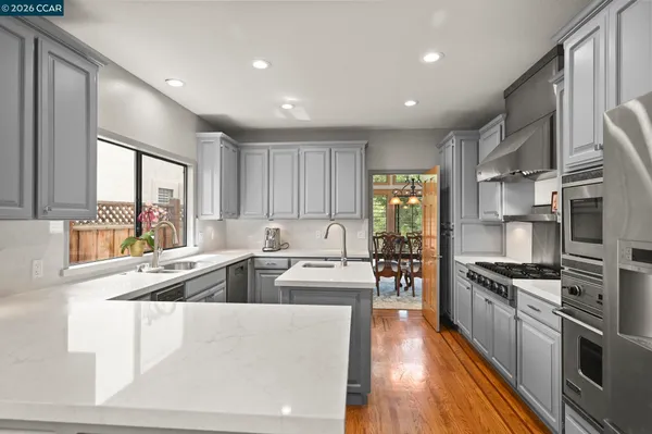 a kitchen with stainless steel appliances granite countertop a stove top oven a sink dishwasher a refrigerator and white cabinets with wooden floor