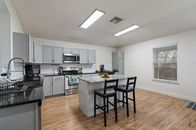 a kitchen with granite countertop a stove top oven a sink dishwasher a dining table and chairs with wooden floor