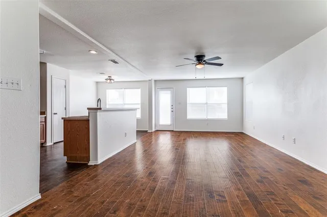 an empty room with wooden floor a ceiling fan and windows