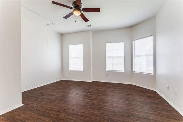 an empty room with wooden floor fan and windows