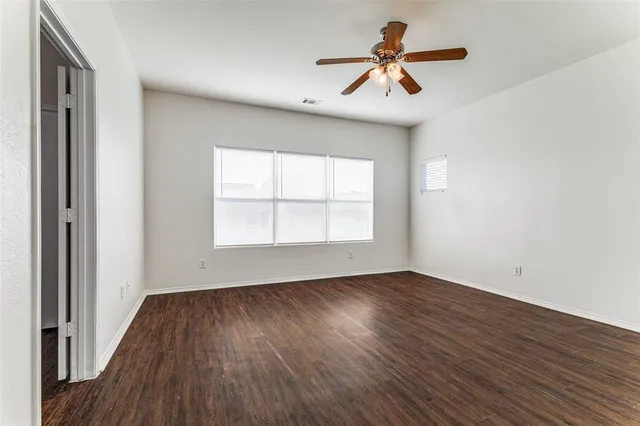 an empty room with wooden floor ceiling fan and windows