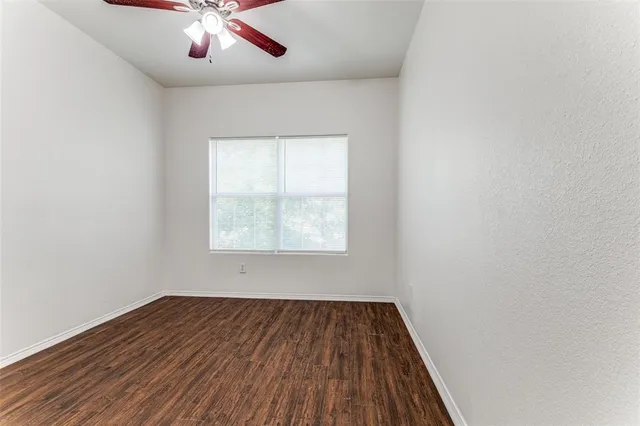 an empty room with wooden floor chandelier fan and windows
