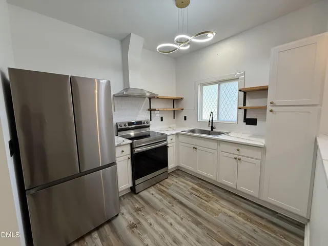 a kitchen with stainless steel appliances granite countertop a refrigerator a sink dishwasher a stove with white cabinets and wooden floor