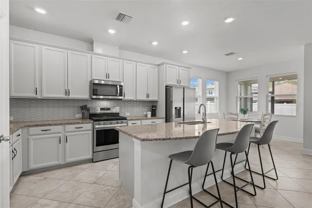 a kitchen with stainless steel appliances granite countertop a stove a sink a microwave a island with a dining table and chairs