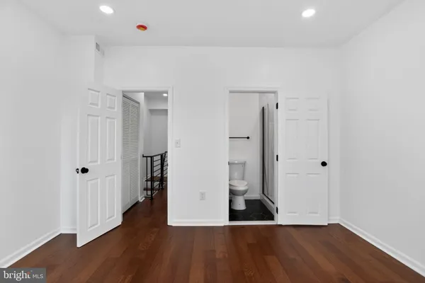 a view of an empty room with wooden floor and a bathroom