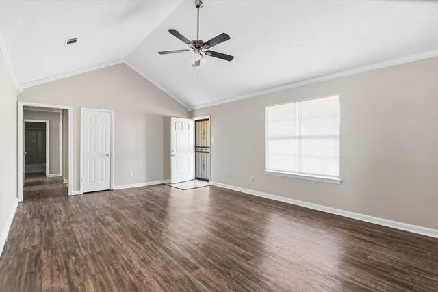 an empty room with wooden floor fan and windows