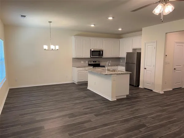 a kitchen with stainless steel appliances granite countertop a stove top oven a refrigerator a sink and a wooden floor