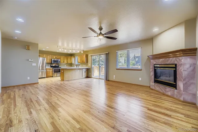 an empty room with wooden floor a kitchen view and a fireplace