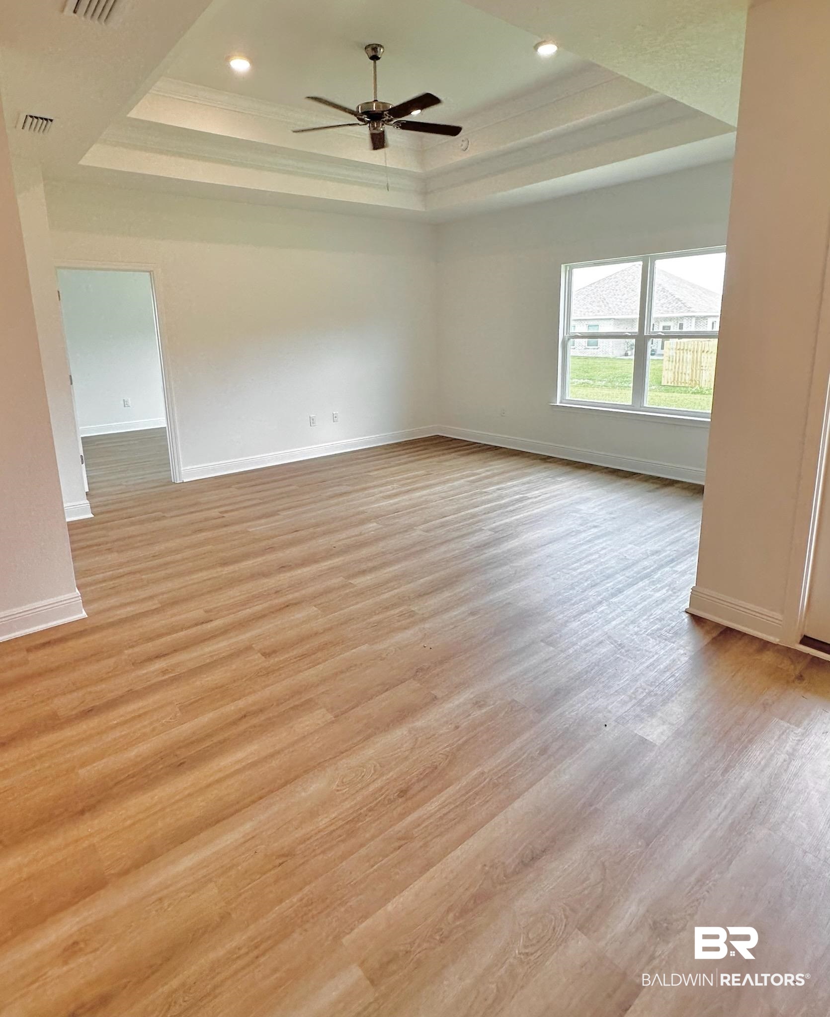 12877 Grand Rpds Road Fairhope, AL 36532 - Photo 7 of 31 Empty room with ceiling fan, a raised ceiling, and light hardwood / wood-style flooring