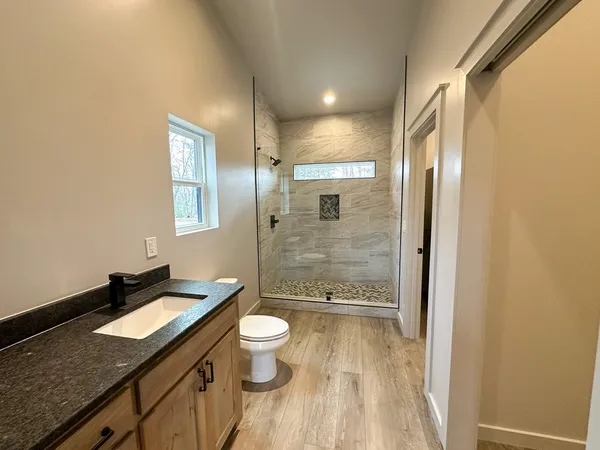 a bathroom with a granite countertop sink a toilet a mirror and shower