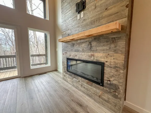 a view of an empty room with wooden floor fireplace and a window