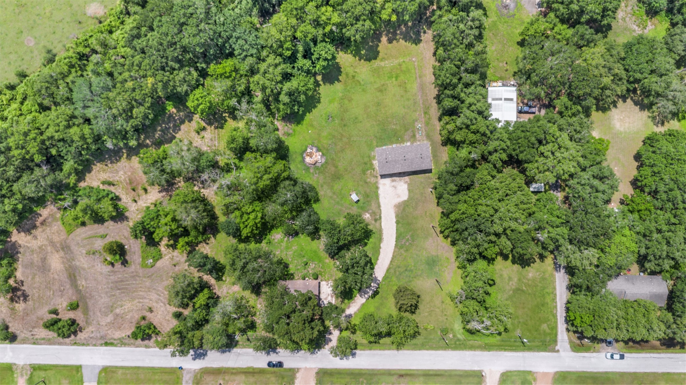 This aerial photo showcases a spacious property with lush greenery, featuring a long driveway leading to a home. The lot is surrounded by trees, providing ample privacy and a serene atmosphere. Ideal for those seeking a blend of nature and convenience.