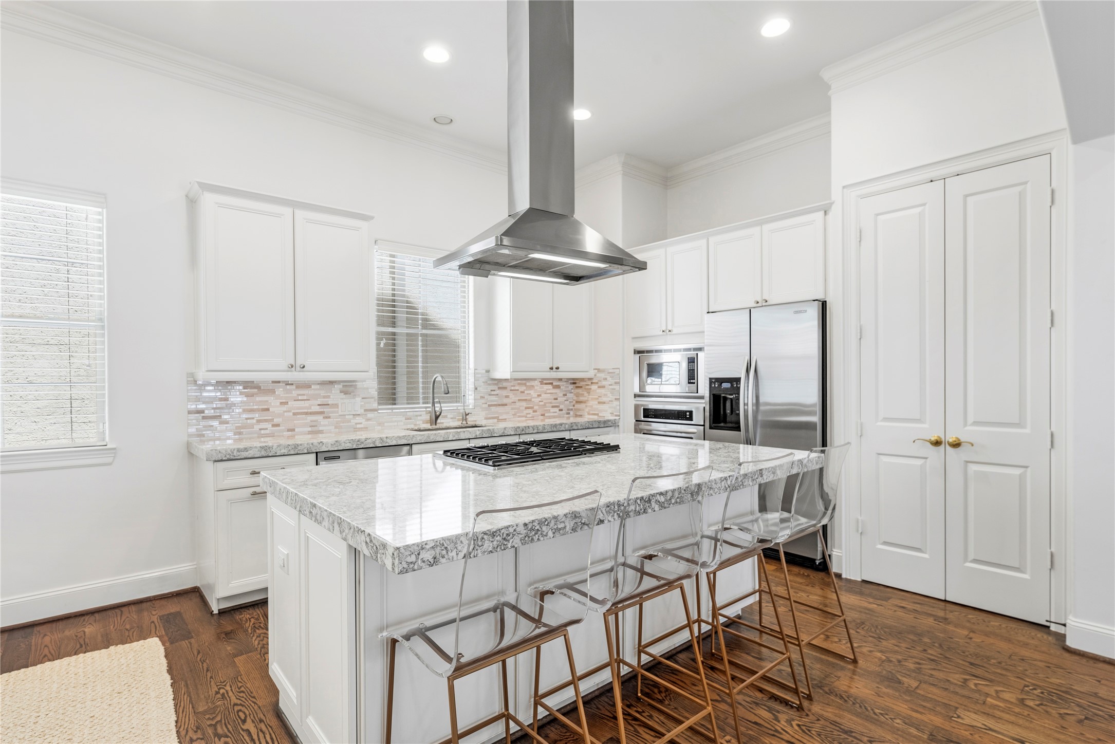 1537 Haddon Street Houston, TX 77006 - Photo 16 of 48 This modern kitchen features sleek white cabinetry, a spacious granite island with seating, stainless steel appliances, and a stylish range hood. The hardwood floors and ample natural light add warmth and brightness to the space.