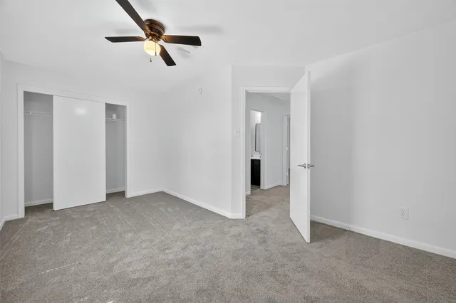 an empty room with a ceiling fan & kitchen view