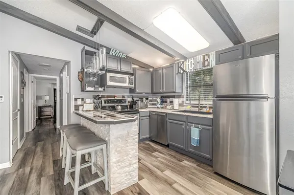 a kitchen with stainless steel appliances granite countertop a refrigerator a sink dishwasher a stove and white cabinets with wooden floor