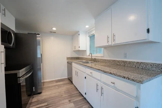 a kitchen with granite countertop a sink stainless steel appliances and white cabinets