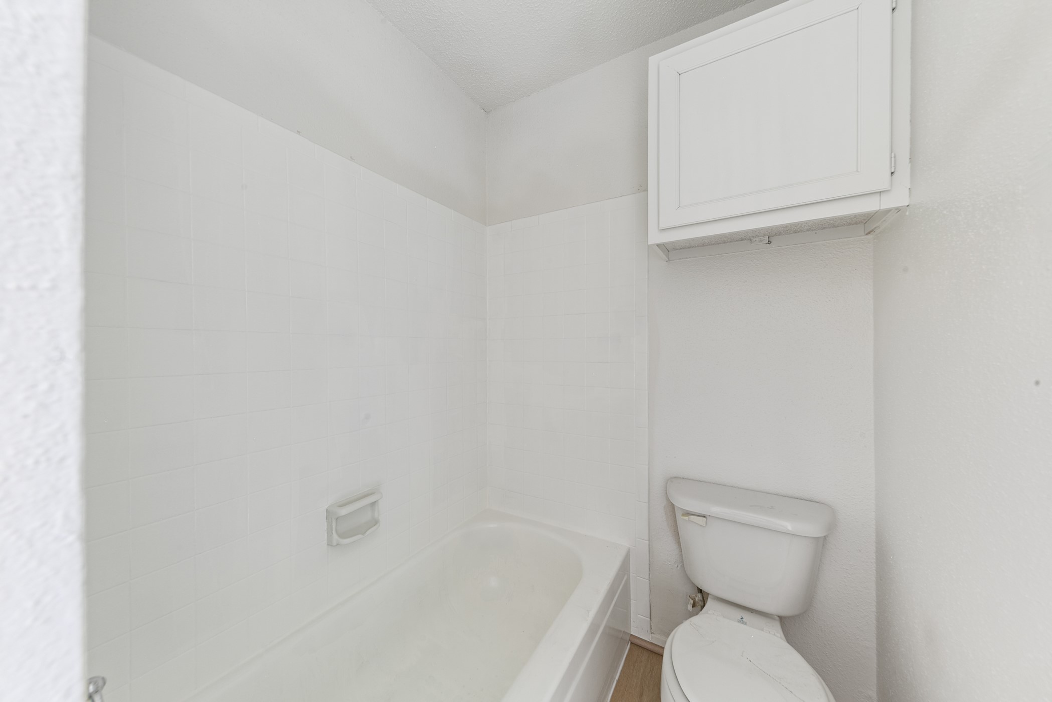700 Lyle W Avenue, Unit D Cleveland, TX 77327 - Photo 8 of 16 This bathroom features a clean, white design with a bathtub, compact toilet, and a wall-mounted cabinet for storage, providing a simple and functional space.