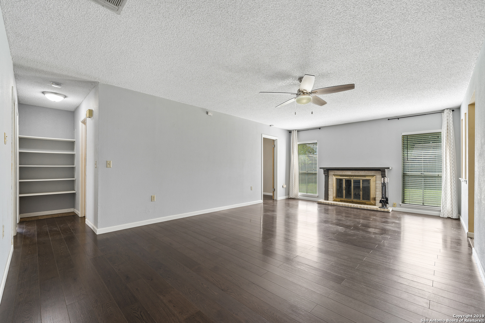 109 Meadow Way Converse, TX 78109 - Photo 6 of 25 an empty room with wooden floor a ceiling fan a fireplace and windows