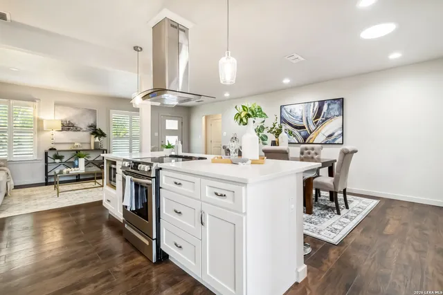 a kitchen with kitchen island granite countertop a stove a sink a dining table and chairs with wooden floor