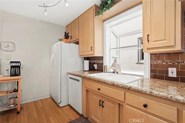 a kitchen with granite countertop a refrigerator a sink and dishwasher with wooden floor