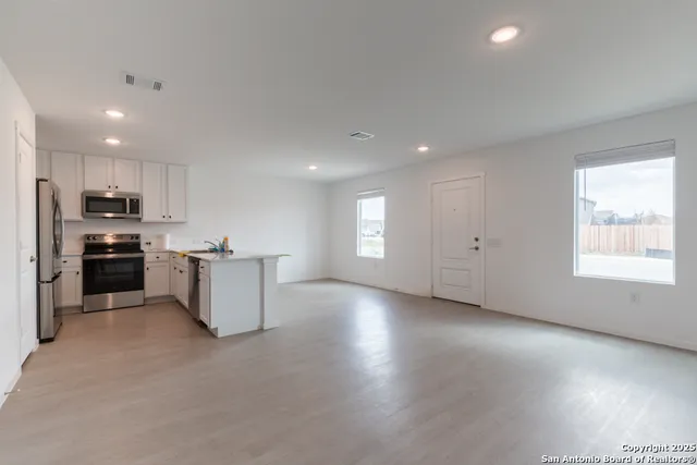 a large kitchen with stainless steel appliances granite countertop a stove a sink a refrigerator and white cabinets with wooden floor