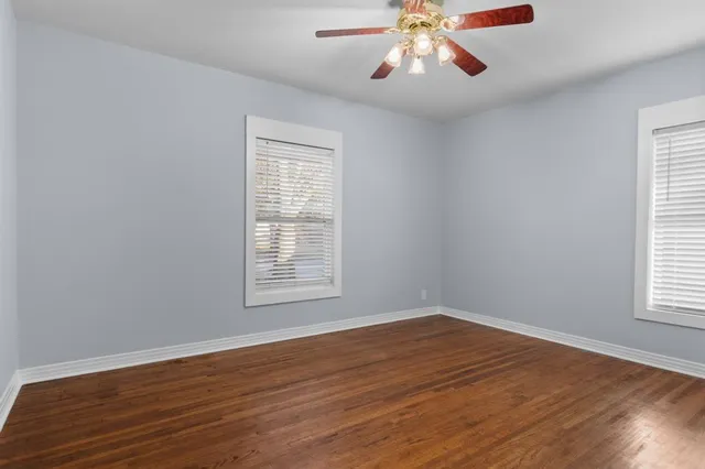 an empty room with wooden floor chandelier fan and windows