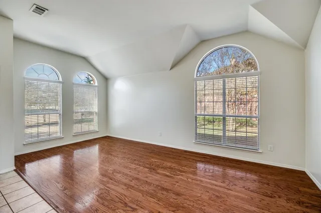 an empty room with wooden floor windows mirror and windows