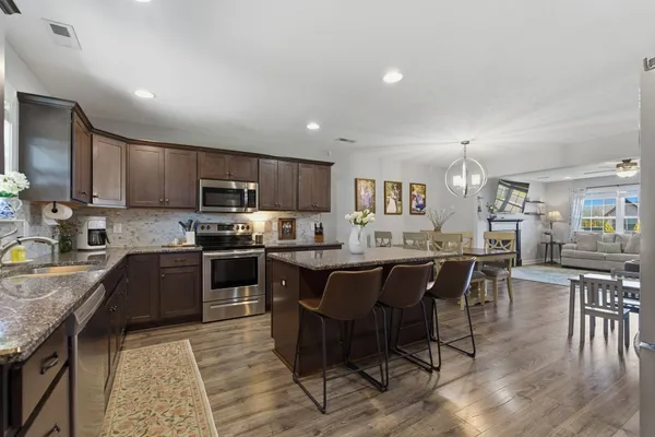 a kitchen with stainless steel appliances granite countertop wooden cabinets a dining table and chairs