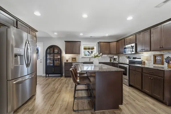 a kitchen with stainless steel appliances granite countertop a refrigerator a stove top oven a sink and dishwasher with wooden floor